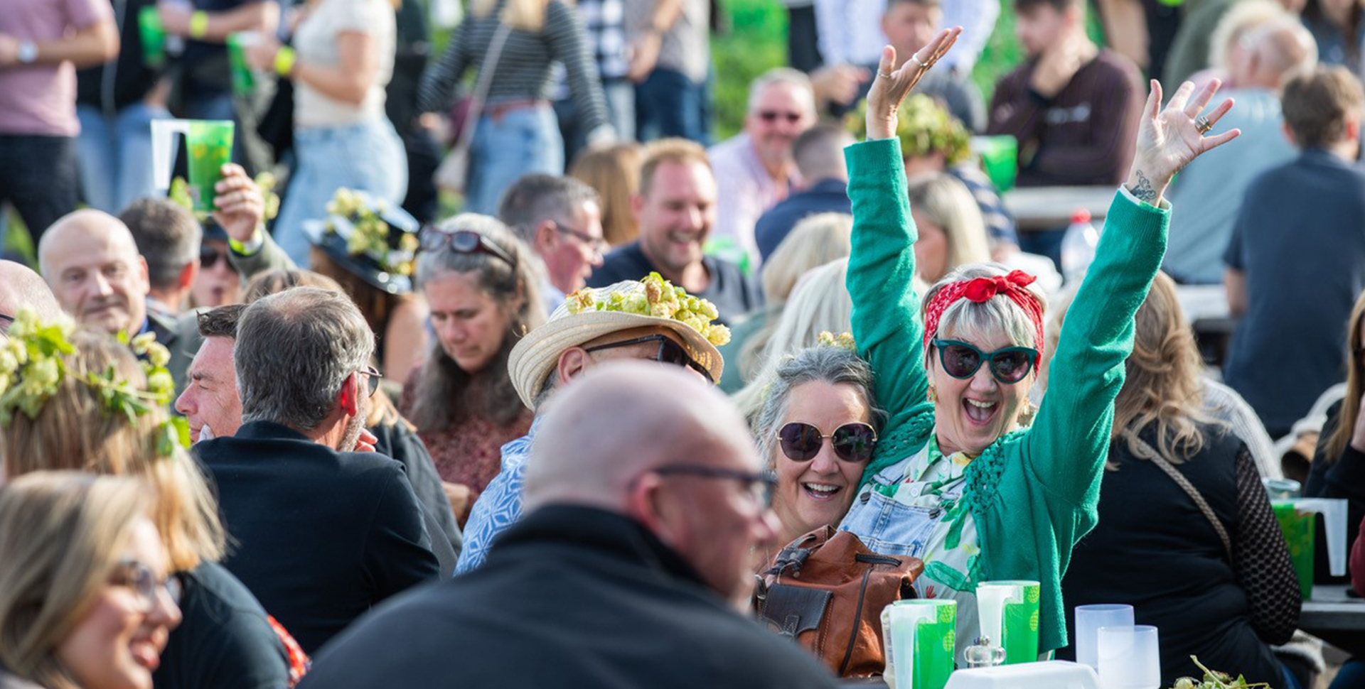 A woman cheering and a woman smiling whilst sitting at an outdoor table full of other people